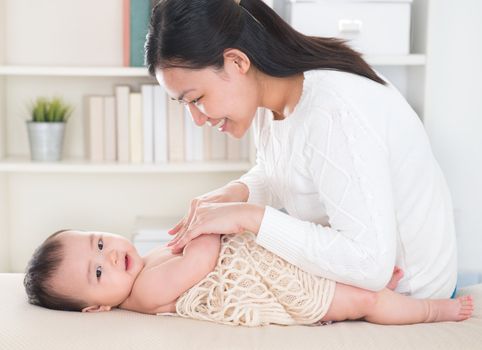 Asian mother giving massage to baby girl at home.
