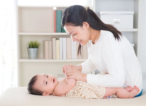 Baby massage. Asian mother massaging baby hands at home.