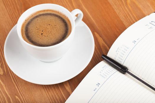 Notebook with pen and cup of coffee on a table. Top view