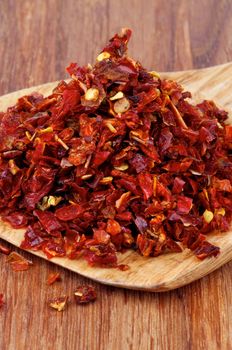 Heap of Dried Paprika with Seeds in Wooden Spoon closeup on Wooden background