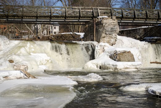 river waterfall retro bridge covered with frozen ice snow and icicles in winter.