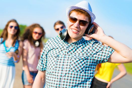 young man in sunglasses, headphones holds a hand on a background of blue sky and friends