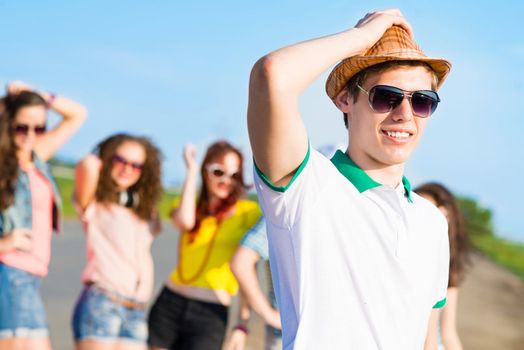 young man in sunglasses, a hat holds a hand on a background of blue sky and friends