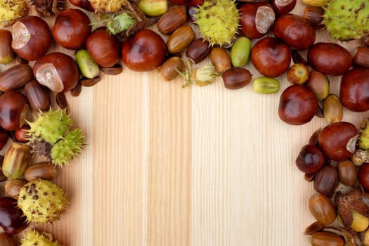 Three-sided border of natural autumn material - acorns, conkers, beechnuts and cobnuts on a wooden background with copy space