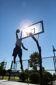 A young basketball player going up for a dunk.  Intentionally back lit with bright lens flare coming through the clear backboard.