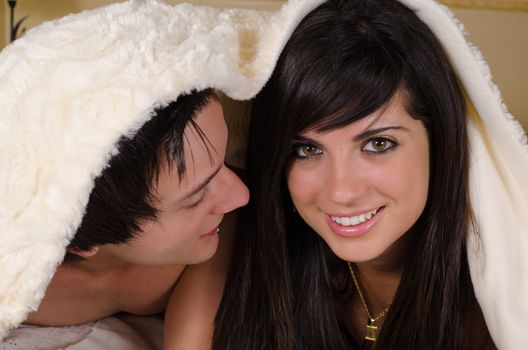 Happy couple  under a cozy blanket looking at camera