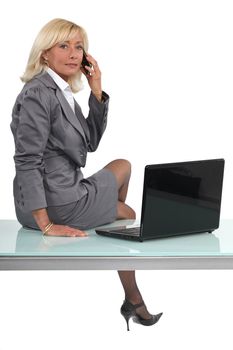 Blond executive sat on desk making call