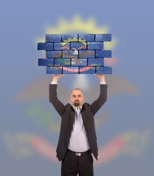 Businessman holding a large piece of a brick wall, flag of North Dakota, isolated on national flag