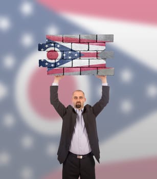 Businessman holding a large piece of a brick wall, flag of Ohio, isolated on national flag