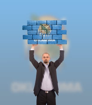 Businessman holding a large piece of a brick wall, flag of Oklahoma, isolated on national flag