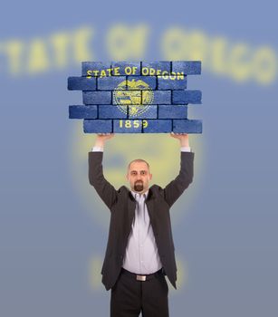 Businessman holding a large piece of a brick wall, flag of Oregon, isolated on national flag