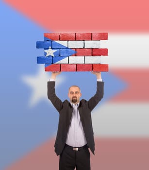 Businessman holding a large piece of a brick wall, flag of Puerto Rico, isolated on national flag