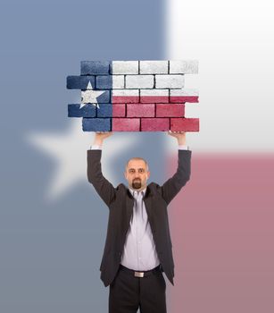 Businessman holding a large piece of a brick wall, flag of Texas, isolated on national flag