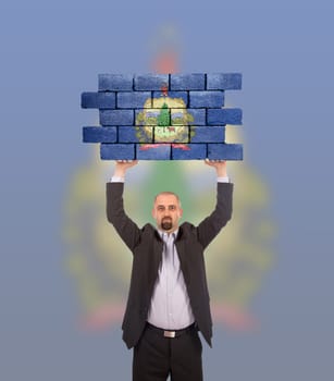 Businessman holding a large piece of a brick wall, flag of Vermont, isolated on national flag