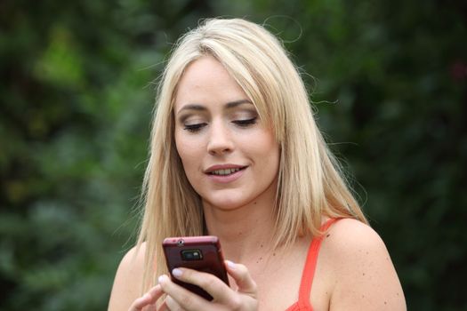 Attractive young blond woman reading an sms on her mobile phone while enjoying a summer day in the park