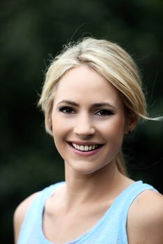 Pretty young blond woman with a natural smile wearing a casual sleeveless summer top outdoors in the garden