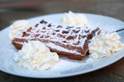 Delicious freshly baked waffle sprinkled with sugar and served on a plate with four dollops of whipped cream