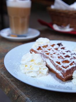 Close up view of a freshly baked golden waffle with whipped cream served on a plate for a tasty dessert