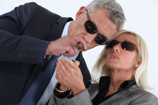 mature gentleman smoking cigar with blonde spouse showing off