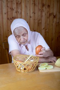 The old woman touches onions sitting at a table