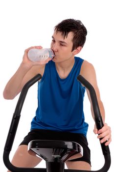 A teenage boy using an exercise bike for fitness.  He is drinking water.  White background.