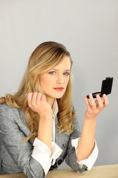 Gorgeous woman in a trendy suit fixing her makeup with a compact