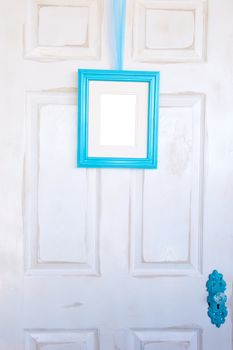 Blank turquoise picture frame hanging by a ribbon of tulle on a distressed white door