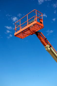 Orange hydraulic utility lift used in the construction industry shot against a blue sky with white clouds