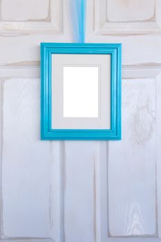 Distressed white door with a blank, turquoise picture frame hanging on it.