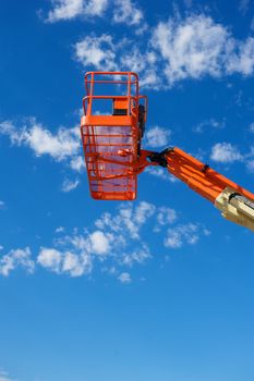 Orange hydraulic utility lift used in the construction industry shot against a blue sky with white clouds