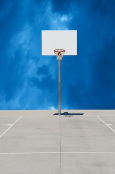 Pure white basketball backboard or standard with orange rim and white net on a gray concrete surface with a blue cloudy background