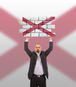 Businessman holding a large piece of a brick wall, flag of Alabama, isolated on national flag