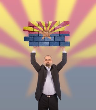 Businessman holding a large piece of a brick wall, flag of Arizona, isolated on national flag