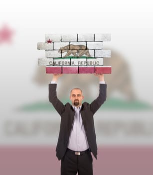 Businessman holding a large piece of a brick wall, flag of California, isolated on national flag