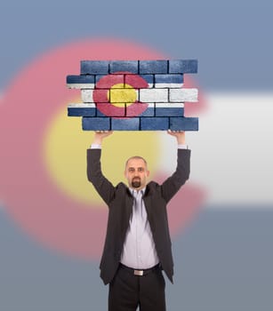 Businessman holding a large piece of a brick wall, flag of Colorado, isolated on national flag