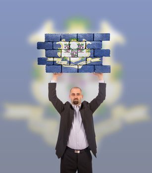 Businessman holding a large piece of a brick wall, flag of Connecticut, isolated on national flag