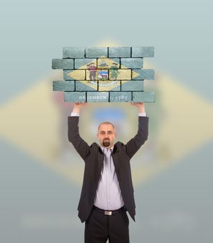 Businessman holding a large piece of a brick wall, flag of Delaware, isolated on national flag