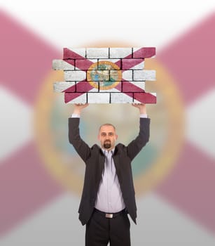 Businessman holding a large piece of a brick wall, flag of Florida, isolated on national flag