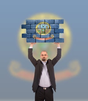 Businessman holding a large piece of a brick wall, flag of Idaho, isolated on national flag