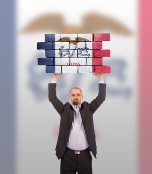 Businessman holding a large piece of a brick wall, flag of Iowa, isolated on national flag