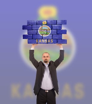 Businessman holding a large piece of a brick wall, flag of Kansas, isolated on national flag