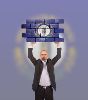 Businessman holding a large piece of a brick wall, flag of Kentucky, isolated on national flag