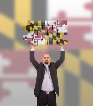 Businessman holding a large piece of a brick wall, flag of Maryland, isolated on national flag