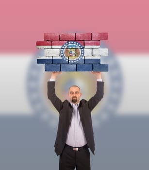 Businessman holding a large piece of a brick wall, flag of Missouri, isolated on national flag