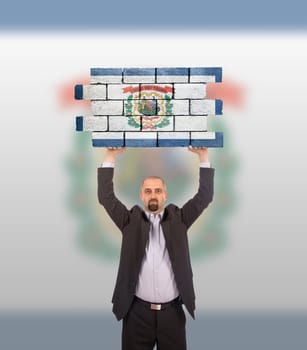 Businessman holding a large piece of a brick wall, flag of West Virginia, isolated on national flag