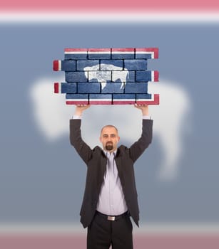 Businessman holding a large piece of a brick wall, flag of Wyoming, isolated on national flag