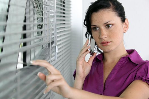 A brunette businesswoman peeping through the blinds.