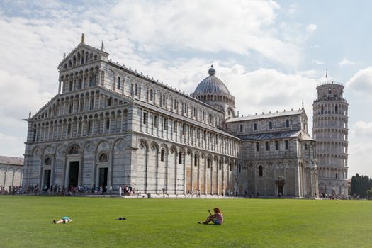 Pisa, Italy – July 11, 2013: View at the Pisa Cathedral and the free-standing bell tower known as the Leaning Tower of Pisa, situated on the Piazza dei Miracoli (Square of Miracles) in the Tuscany city of Pisa, Italy, with crowds of tourists strolling around.