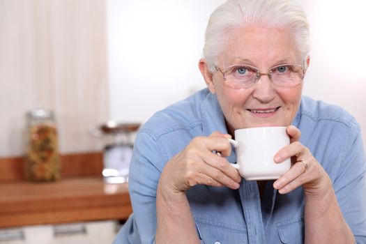 Elderly lady enjoying cup of tea in her kitchen