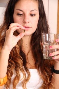 A young woman taking a pill with a glass of water.